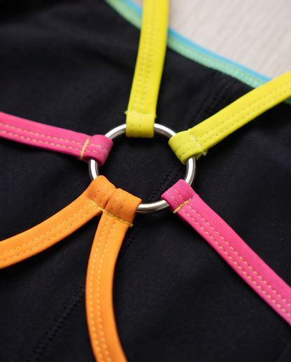Close-up of the back of our custom leo with a central silver metal ring and five brightly colored straps radiating from it: yellow, pink, orange, and two teal-blue straps.