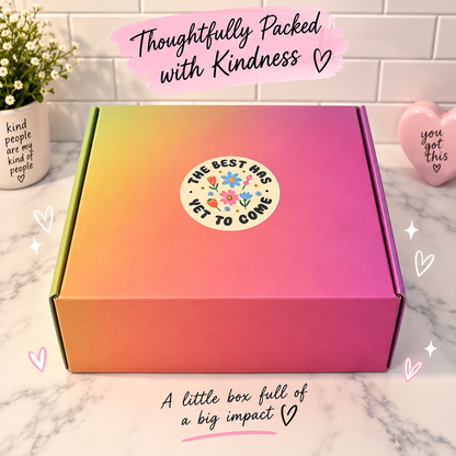 A pastel gradient cardboard box with a colorful floral sticker reading 'THE BEST HAS YET TO COME' sits on a marble countertop. The box shows a green-to-yellow-to-pink-to-orange gradient.