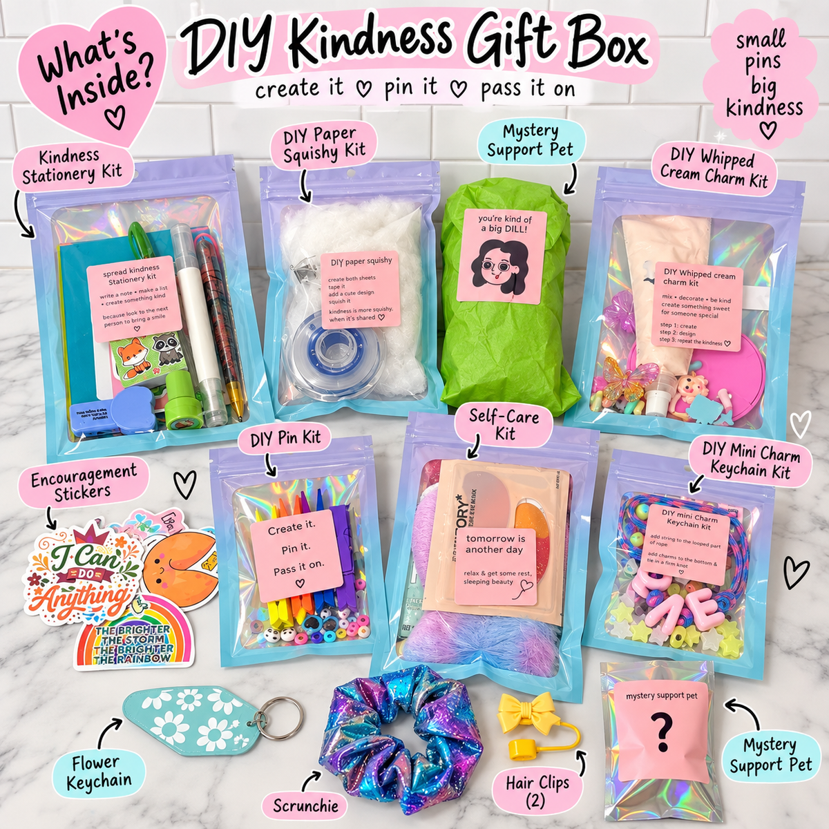 A DIY Kindness Gift Box set arranged on a white marble background, featuring multiple zippered pouches with colorful contents including pens, glitter, cream chalk, a mystery pet photo, stickers, keychains, scrunchies, and hair clips. Text labels identify each included kit, and the top header reads 'DIY Kindness Gift Box create it ♥ pin it ♥ pass it on'.
