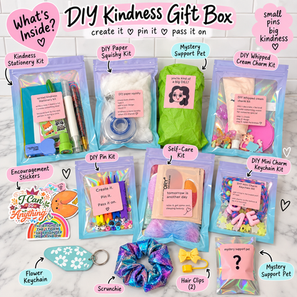A DIY Kindness Gift Box set arranged on a white marble background, featuring multiple zippered pouches with colorful contents including pens, glitter, cream chalk, a mystery pet photo, stickers, keychains, scrunchies, and hair clips. Text labels identify each included kit, and the top header reads 'DIY Kindness Gift Box create it ♥ pin it ♥ pass it on'.